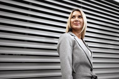 Şehirde dolaşan gri takım elbiseli genç sarışın iş kadını portresi.