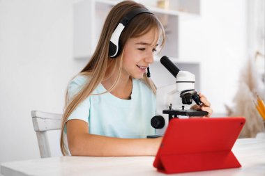 Evde online ders sırasında mikroskop kullanan genç bir kız.