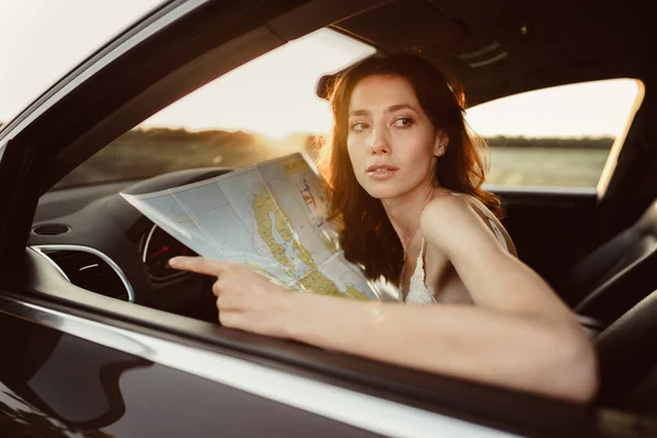 Verlorene junge Frau sitzt in ihrem Auto auf dem Land und schaut auf Landkarte — Stockfoto