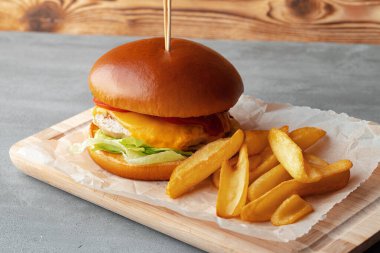Gri ahşap arka planda taze hamburger ve patates dilimleri.