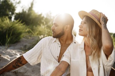 Kumsalda yan yana oturan genç çift.