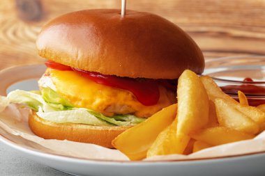 Gri ahşap arka planda taze hamburger ve patates dilimleri.