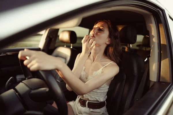 Schöne junge Kaukasierin bemalt Lippen auf dem Beifahrersitz ihres Autos — Stockfoto