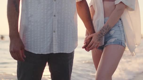 Couple méconnaissable tenant la main sur le bord de la mer au coucher du soleil gros plan — Video