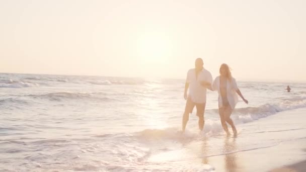 Coppia di giovani amanti che si tengono per mano passeggiando lungo la spiaggia in riva al mare — Video Stock