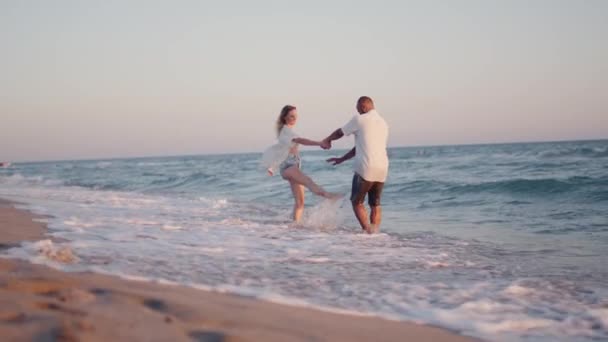 Coppia di giovani amanti che si tengono per mano passeggiando lungo la spiaggia in riva al mare — Video Stock