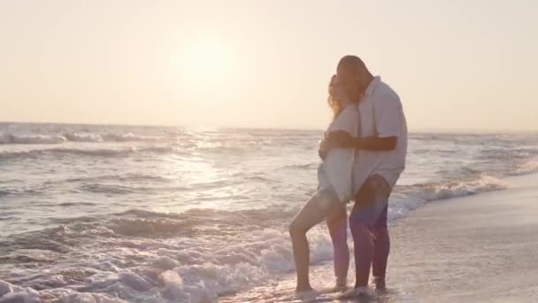 Молодая красивая пара влюблена стоя и обнимаясь на пляже у моря — стоковое видео