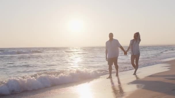 Coppia di giovani amanti che si tengono per mano passeggiando lungo la spiaggia in riva al mare — Video Stock