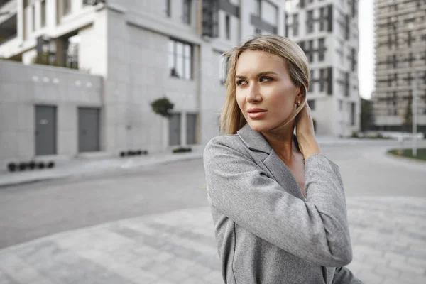 Retrato de una joven empresaria rubia en traje gris caminando por la ciudad — Foto de Stock