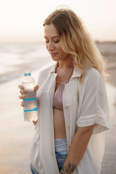 Молода жінка п'є воду з пляшки на пляжі — стокове фото