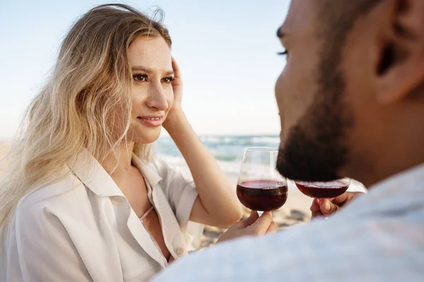 Retrato de una joven pareja sentada en la playa y bebiendo vino — Foto de Stock