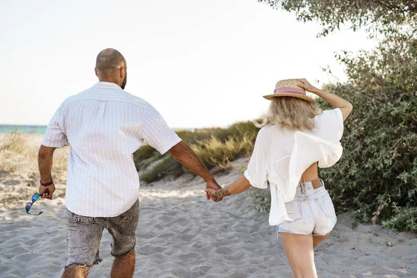 若い幸せなカップルが手を取り合い、夏の日にビーチに一緒に歩く — ストック写真