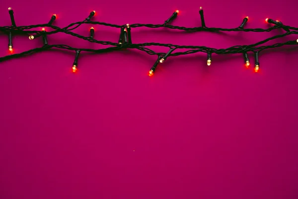 Luces de guirnalda iluminadas sobre fondo rosa brillante — Foto de Stock