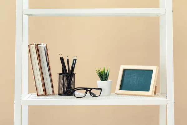 Estante branca com livros e artigos de papelaria contra a parede bege — Fotografia de Stock