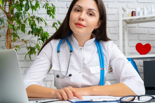 Ung kvinnlig läkare kardiolog sitter vid sitt skrivbord och arbetar — Stockfoto