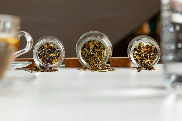 Glazen potten met droge theeblaadjes close-up op witte tafel — Stockfoto