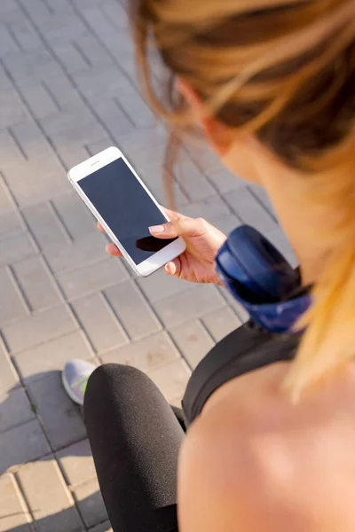 Attractive sporty woman using smartphone with headphones in the morning park — Stock Photo, Image