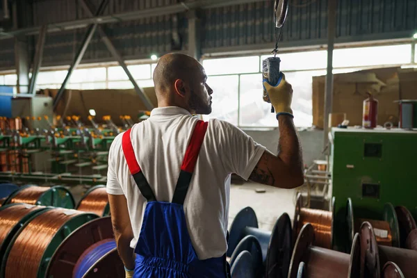 Egyenruhás mérnök daru vezérlővel lóg a mennyezetről egy gyárban — Stock Fotó