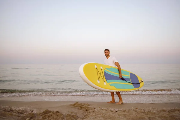 Young man carrying sup board after water surf session — Stock Photo, Image