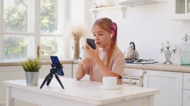 Genç bir kız, mutfakta akıllı telefonuyla video görüşmesi yapıyor.