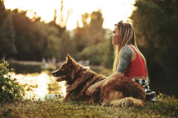 Primer plano de la joven hembra con su perro sentado en la hierba en el parque — Foto de Stock