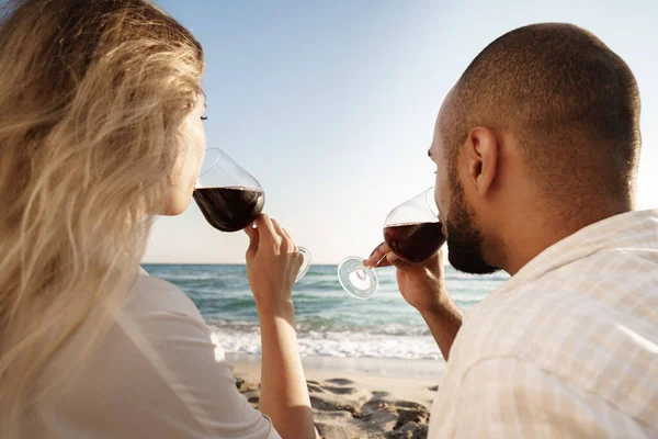 Retrato de um jovem casal sentado na praia e bebendo vinho — Fotografia de Stock