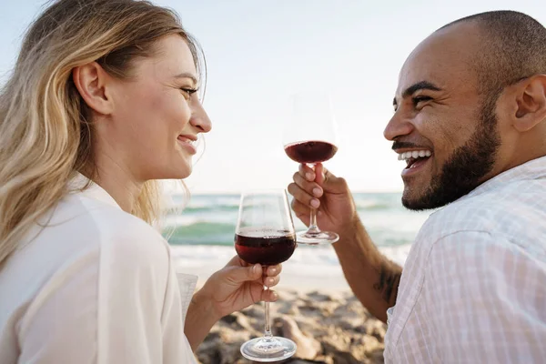 Retrato de una joven pareja sentada en la playa y bebiendo vino — Foto de Stock