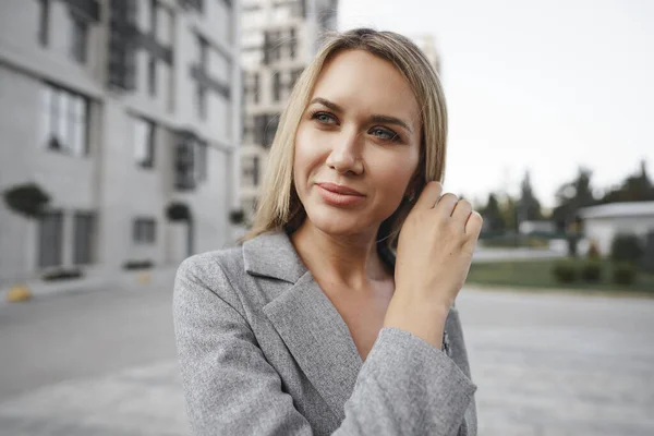 Ritratto di giovane donna d'affari bionda in abito grigio che cammina in città — Foto Stock