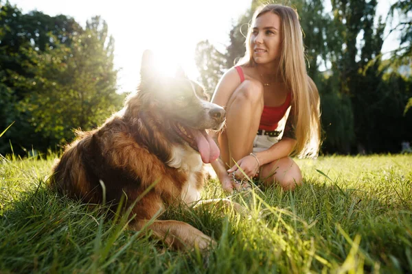 Primer plano de la joven hembra con su perro sentado en la hierba en el parque — Foto de Stock