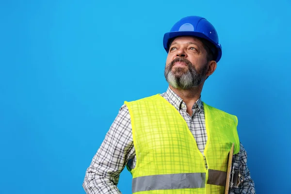 Construtor masculino ou faz-tudo em uniforme segurando prancheta contra fundo azul — Fotografia de Stock