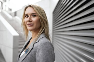 Şehirde dolaşan gri takım elbiseli genç sarışın iş kadını portresi.