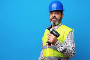 Mavi şapkalı tamirci mavi arka planda tornavida tutuyor.