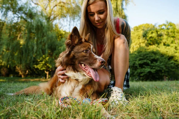 Primer plano de la joven hembra con su perro sentado en la hierba en el parque — Foto de Stock