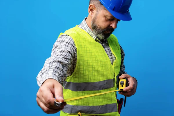 Manlig byggare innehav mätning roulette mot blå bakgrund — Stockfoto