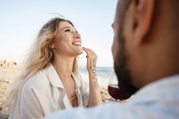 Retrato de una joven pareja sentada en la playa y bebiendo vino — Foto de Stock