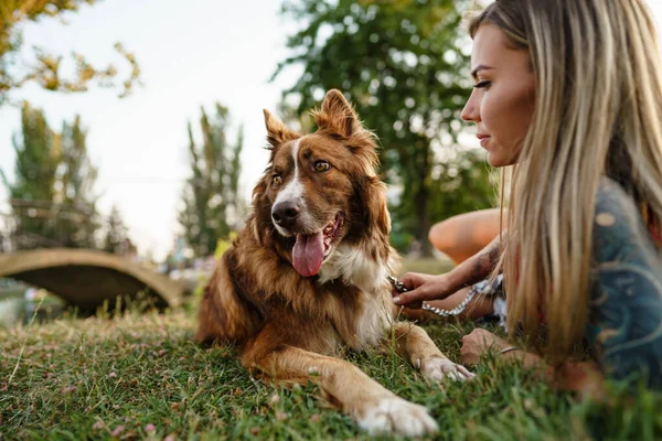 Primer plano de la joven hembra con su perro sentado en la hierba en el parque — Foto de Stock