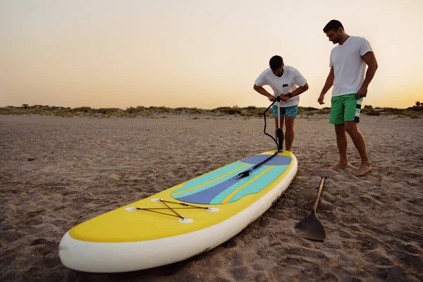 Young man inflating paddle sup board on the beach at sunrise — Stock Photo, Image