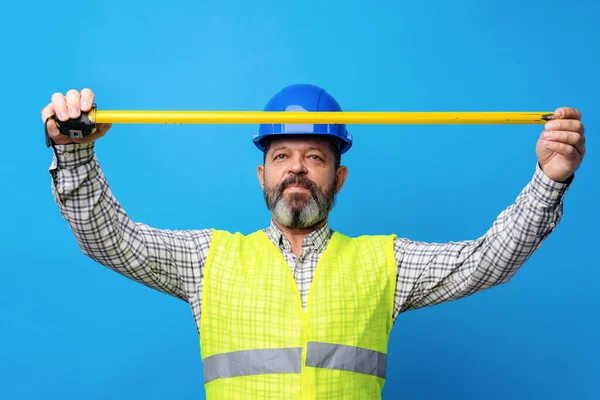 Manlig byggare innehav mätning roulette mot blå bakgrund — Stockfoto