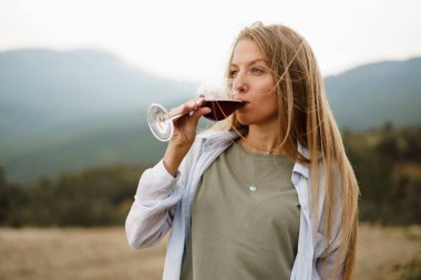 Dağlarda bir bardak kırmızı şarapla güzel genç bir bayan.