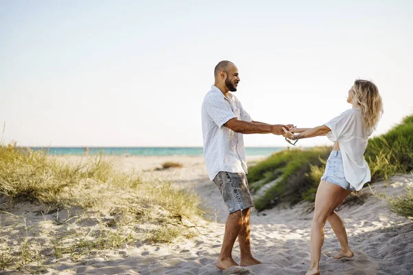 若い幸せなカップルが手を取り合い、夏の日にビーチに一緒に歩く — ストック写真