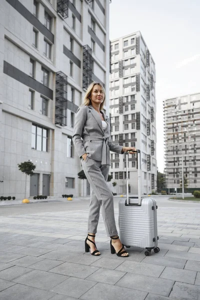 Bizneswoman w szarym garniturze w podróży służbowej spaceru z bagażem w mieście — Zdjęcie stockowe