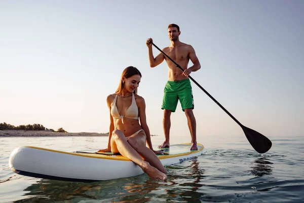 Casal de turistas jovem e mulher se divertindo paddleboarding no mar — Fotografia de Stock