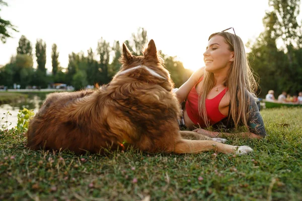 Close up de jovem fêmea com seu cão sentado na grama no parque — Fotografia de Stock