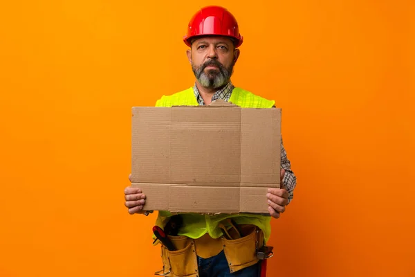 Középkorú építőmunkás egy üres plakáttal narancssárga háttérrel — Stock Fotó