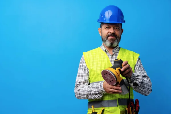 Industribyggare innehav slipmaskin mot blå bakgrund — Stockfoto