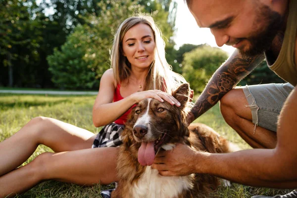 Joven pareja feliz jugando con su perro sonriendo en el parque — Foto de Stock