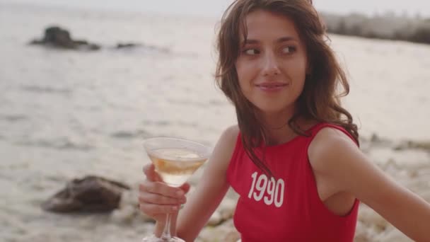 Young brunette woman in red shirt sitting on beach with glass of wine enjoying holidays — Stok Video