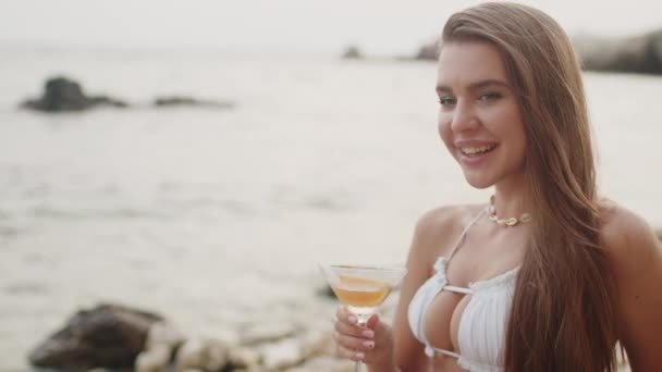 Досить гаряча дівчина з коктейлем сидить на пляжі і купається на курорті — стокове відео