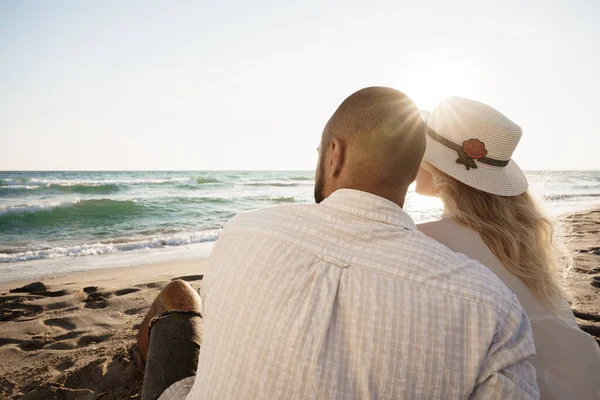 Красивая пара, сидящая на пляже и любующаяся закатом — стоковое фото