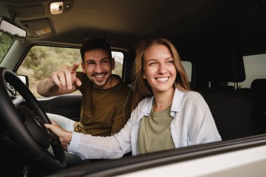Beautiful young couple sitting on front passenger seats and driving a car clipart